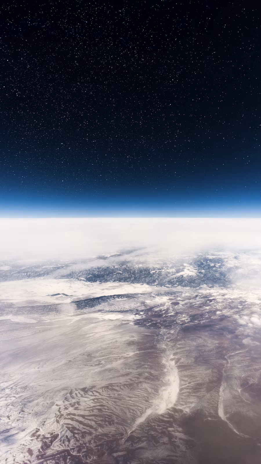 Expansive aerial view of snow-covered mountains and desert landscape beneath a star-filled dark sky.